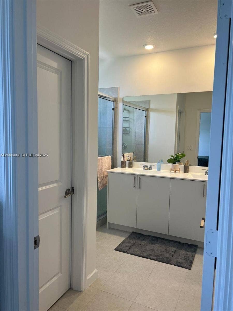 3024 Green Palm Court, #5838, Dania, Dania Beach, FL 33312 Dual-sink vanity with light-toned cabinetry, light-colored countertops, large wall-mounted mirror, and glass-enclosed shower featuring tile surrounds