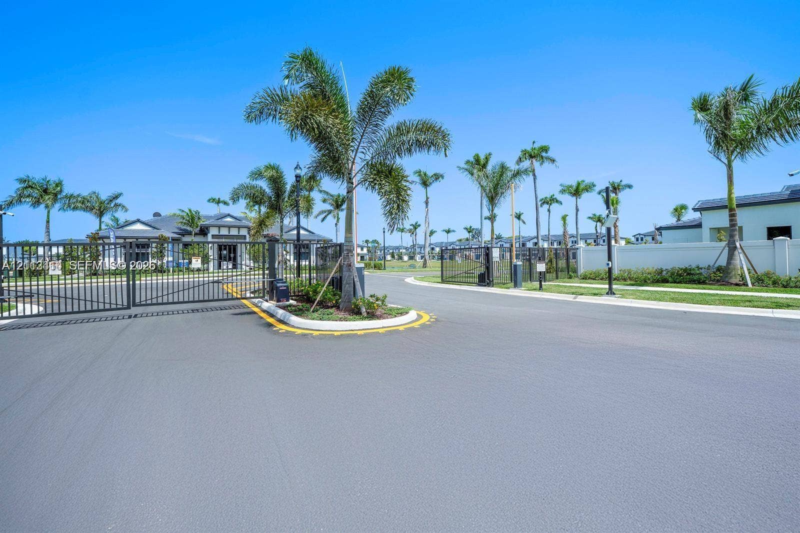 3024 Green Palm Court, #5838, Dania, Dania Beach, FL 33312 Gated community entrance featuring metal perimeter fencing, paved roadway, manicured landscaping, and mature palm trees