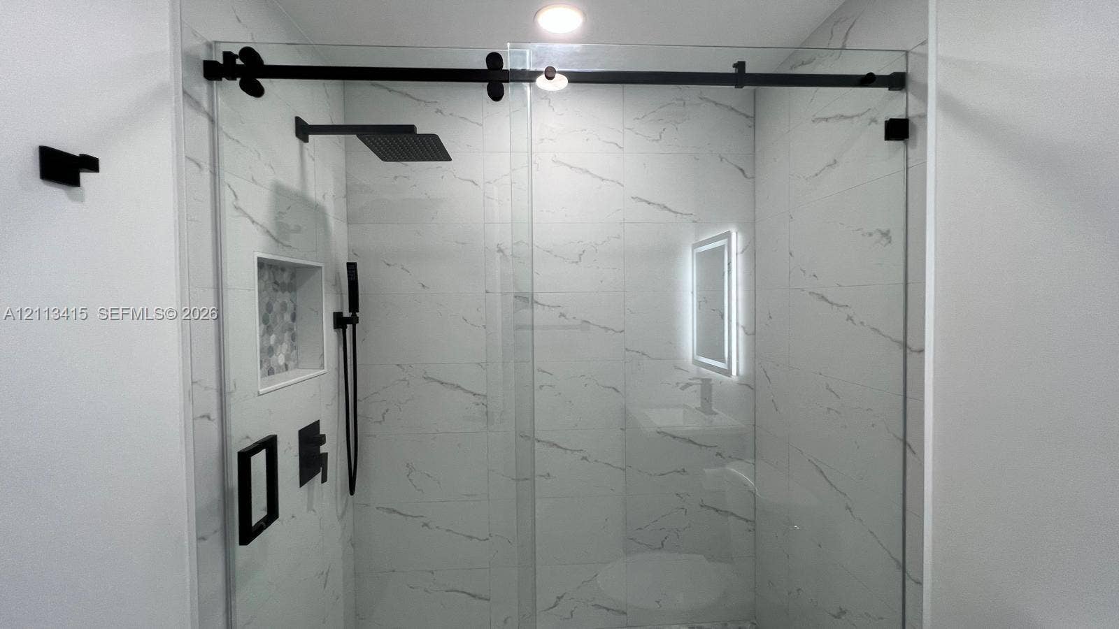 14442 SW 111th Street, #Studio, Miami, Miami, FL 33186 Walk-in shower featuring large-format stone-pattern tile, a glass sliding door with matte black hardware, a rainfall showerhead, and a built-in recessed storage niche
