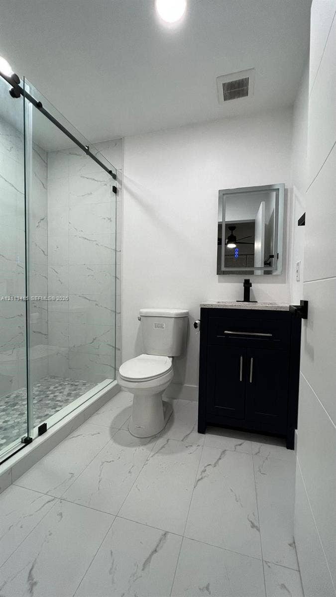 14442 SW 111th Street, #Studio, Miami, Miami, FL 33186 Bathroom featuring large-format tile flooring, a glass-enclosed shower with floor-to-ceiling tile surround and pebble-texture shower floor, dark cabinetry with a stone countertop, and a rectangular-framed vanity mirror
