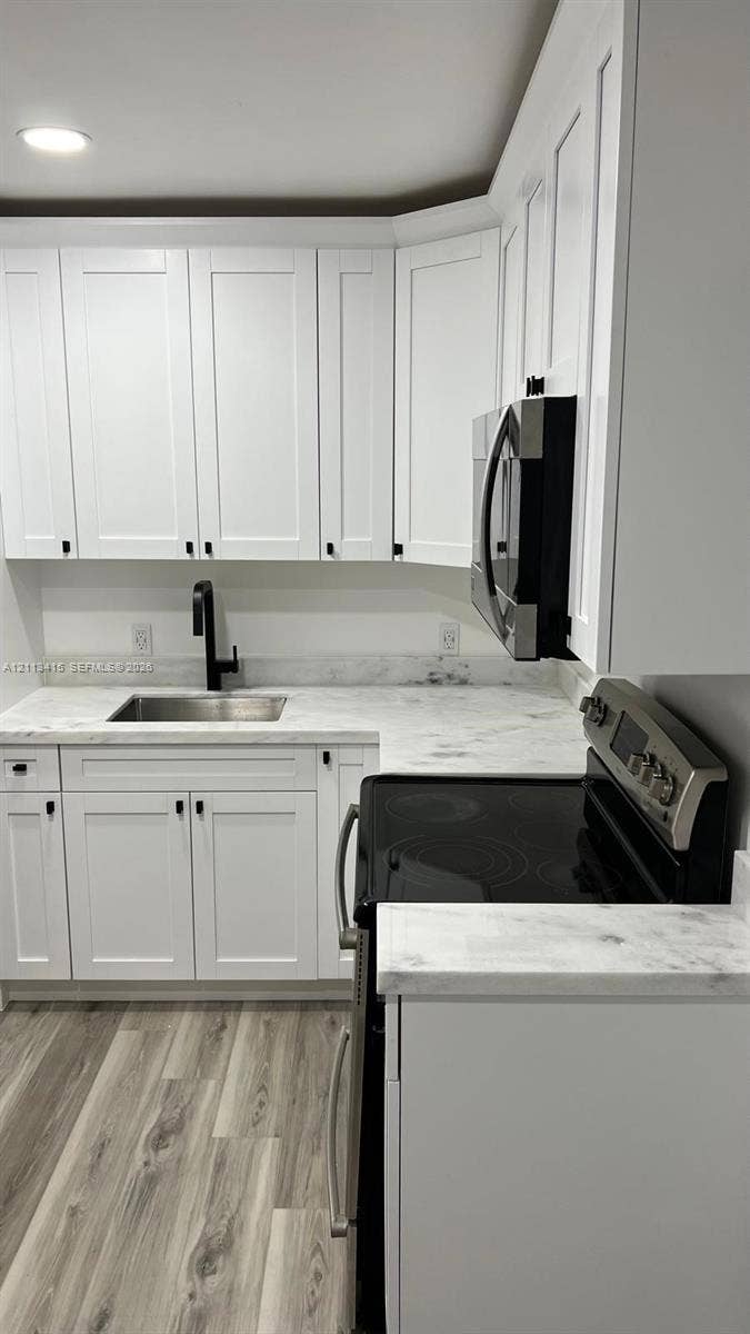 14442 SW 111th Street, #Studio, Miami, Miami, FL 33186 Kitchen featuring white Shaker-style cabinetry, light stone-finish countertops, stainless steel appliances, a matte black faucet, and wood-finish flooring