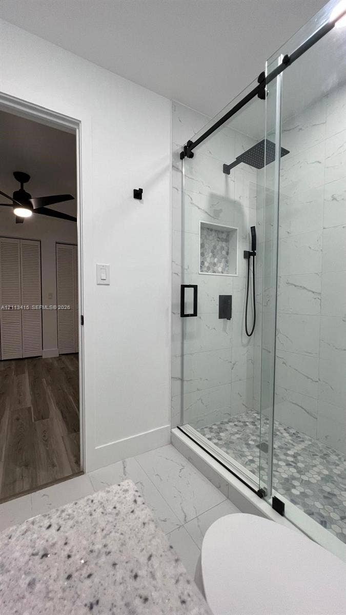 14442 SW 111th Street, #Studio, Miami, Miami, FL 33186 Walk-in shower featuring a glass enclosure with a matte black sliding track, rainfall showerhead, integrated tiled niche, and stone mosaic flooring