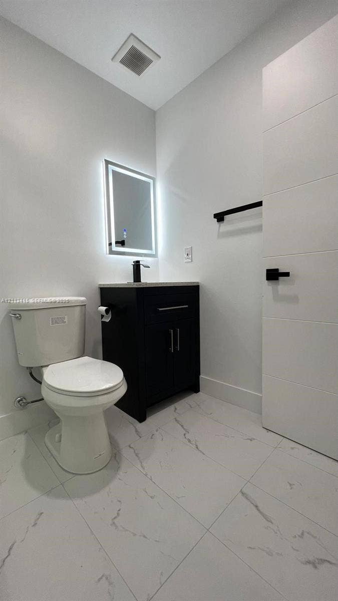 14442 SW 111th Street, #Studio, Miami, Miami, FL 33186 Modern bathroom featuring white tile flooring with grey veining, a dark-finish vanity with a stone countertop, a wall-mounted LED mirror, and matte black fixtures