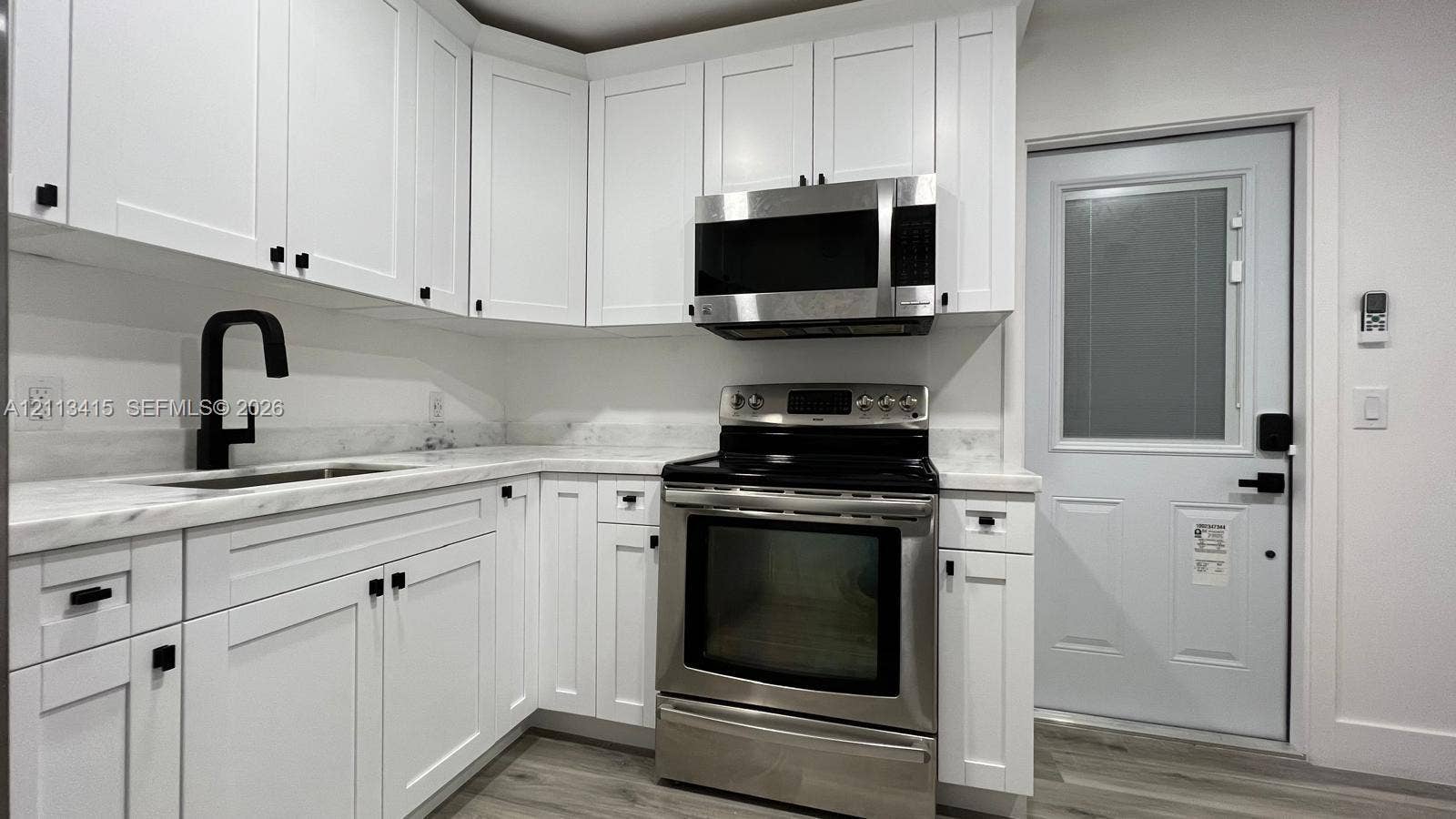 14442 SW 111th Street, #Studio, Miami, Miami, FL 33186 White shaker cabinetry, light-toned stone-finish countertops, stainless steel appliances, matte black hardware, and wood-finish flooring