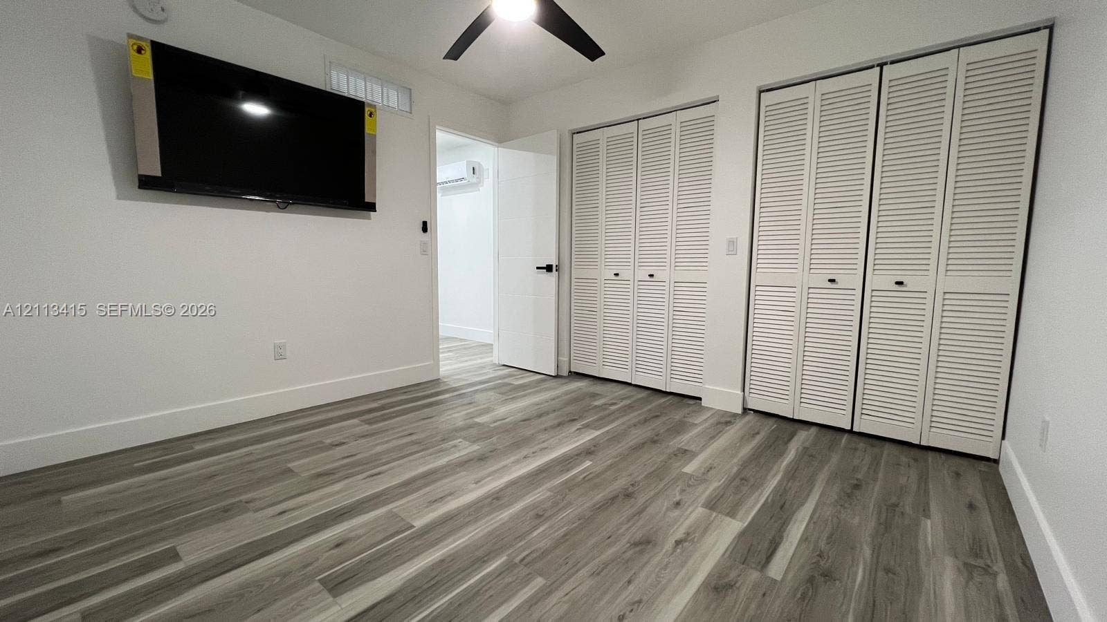 14442 SW 111th Street, #Studio, Miami, Miami, FL 33186 Wood-finish flooring, dual bi-fold louvered closets, matte black ceiling fan, and a wall-mounted ductless air conditioning unit