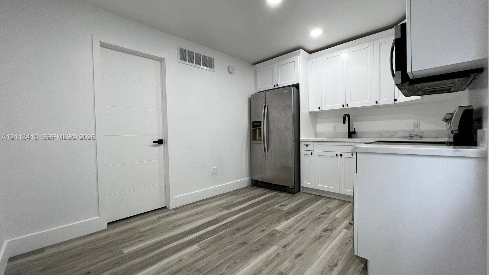 14442 SW 111th Street, #Studio, Miami, Miami, FL 33186 Kitchen featuring white Shaker-style cabinetry, light-toned stone-finish countertops, matte black plumbing fixtures, stainless steel refrigerator, and wood-finish flooring