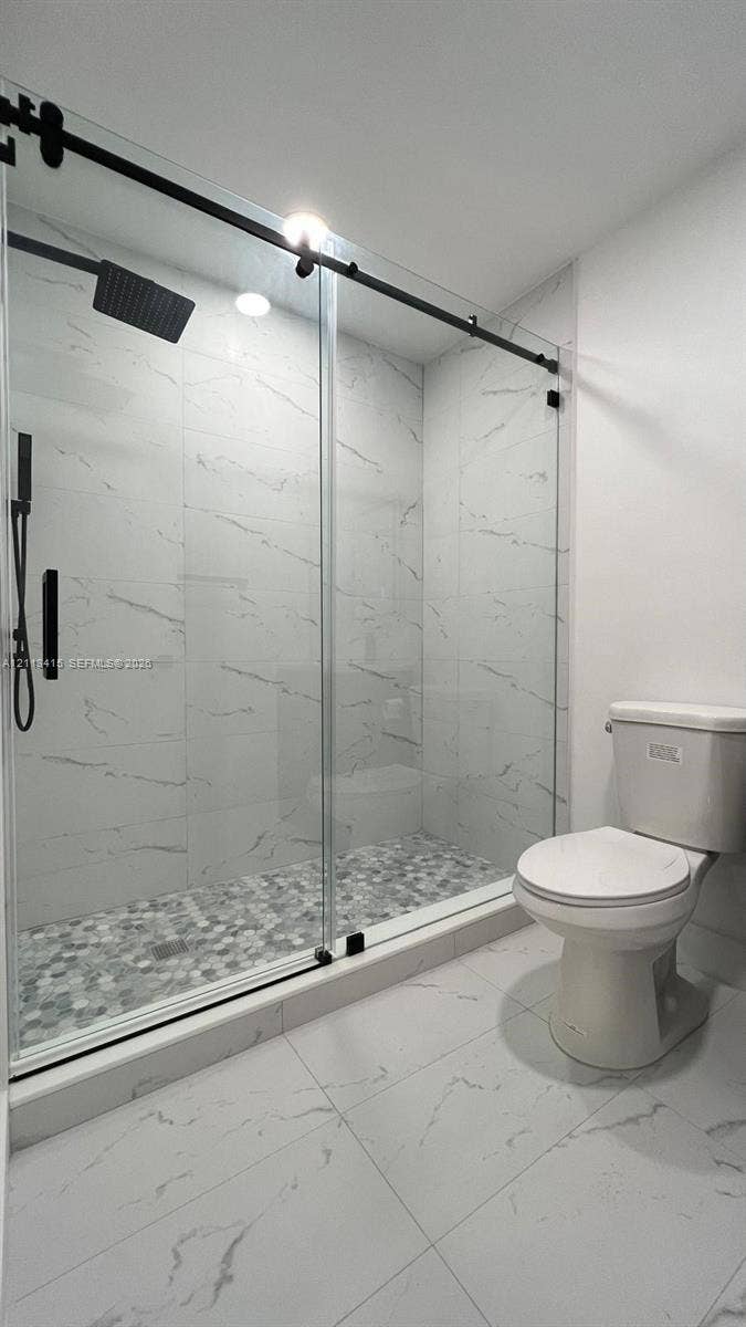 14442 SW 111th Street, #Studio, Miami, Miami, FL 33186 Walk-in shower featuring large-format stone-pattern tile walls, a pebble-finish floor, a matte black sliding glass enclosure, and a rainfall showerhead