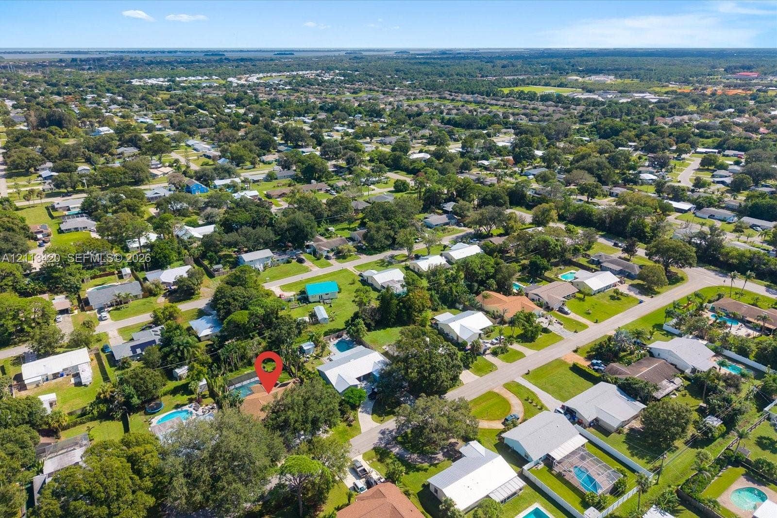 Aerial perspective of the residential property featuring a screened-in pool enclosure, mature canopy trees, and paved street access
