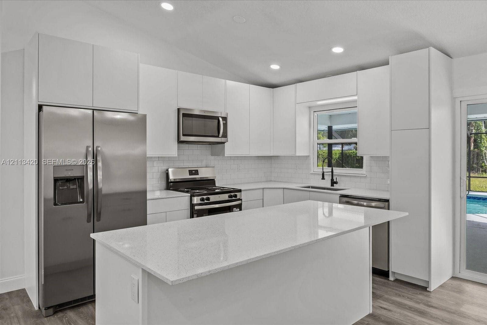 Kitchen featuring flat-panel white cabinetry, a center island with stone-finish countertops, stainless steel appliances, a white subway tile backsplash, and recessed lighting