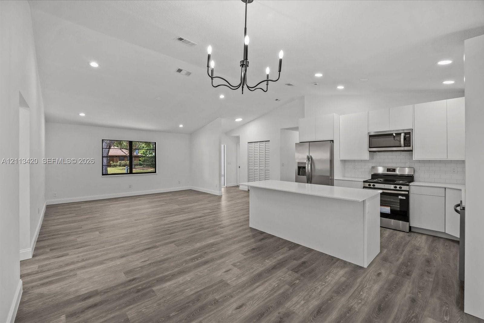 Open-concept interior featuring vaulted ceilings, wood-finish flooring, a central island with a quartz countertop, recessed lighting, and an iron chandelier
