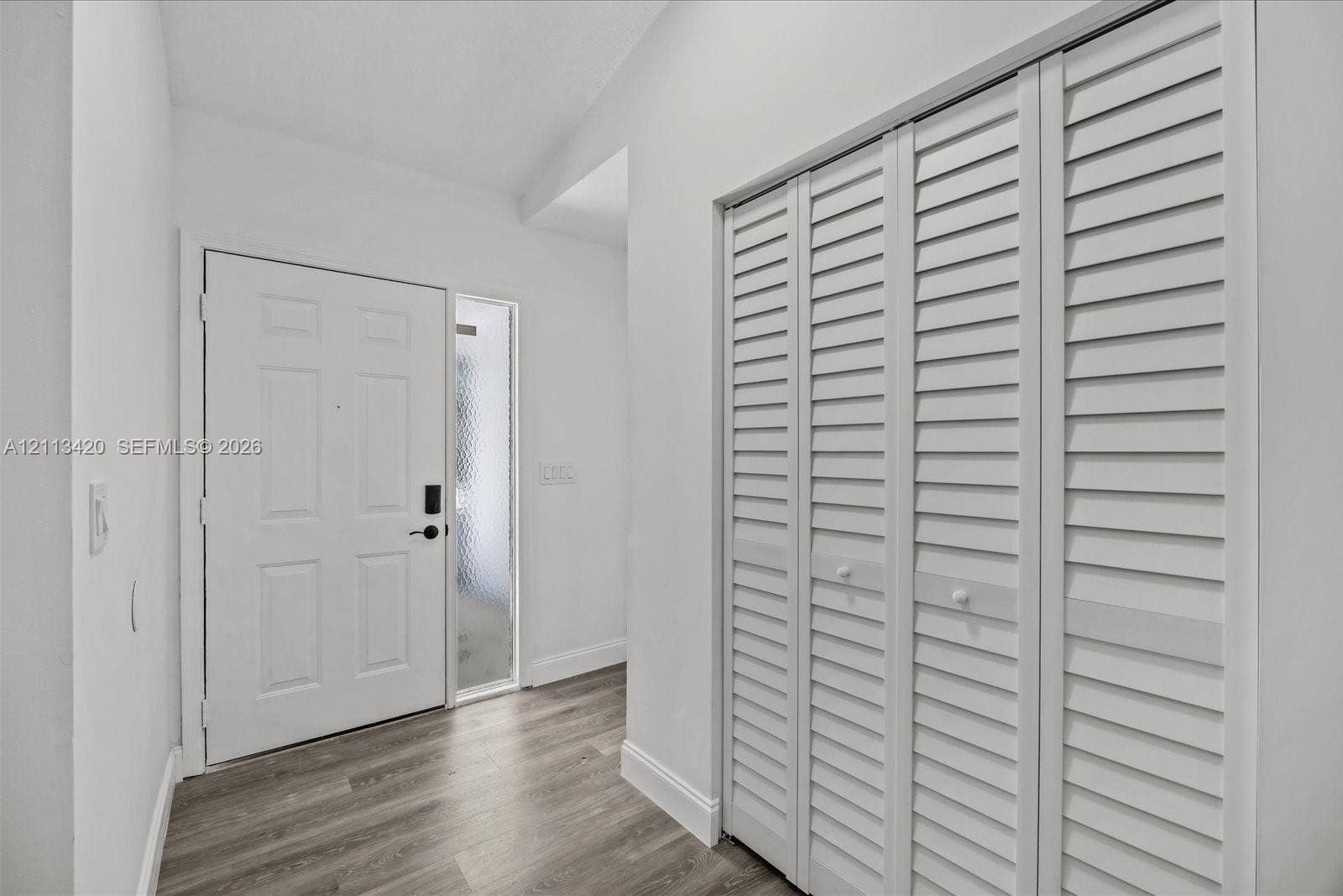 Entryway featuring white-finish louvered bi-fold closet doors, wood-finish flooring, a solid panel entry door, and an adjacent frosted glass sidelight