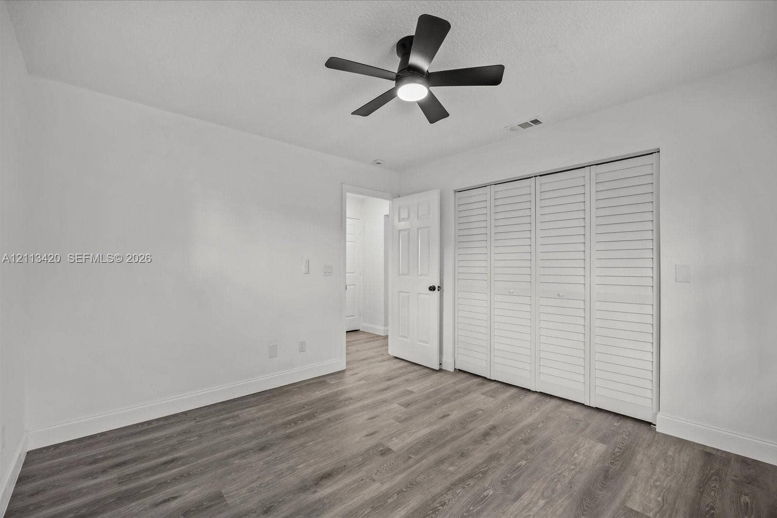 Interior space featuring wood-finish flooring, a matte black multi-blade ceiling fan with integrated light, and a four-panel louvered closet door