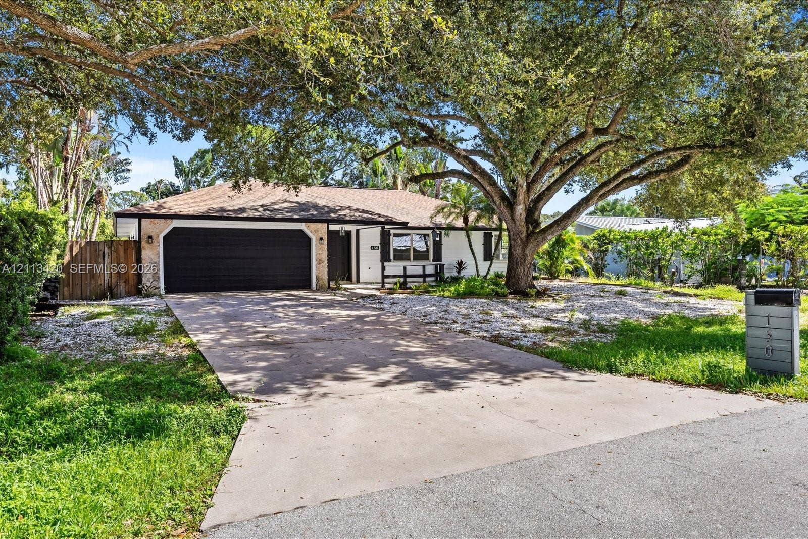 Single-story exterior featuring a concrete driveway, dual-car garage, stone facade accents, and mature shade trees