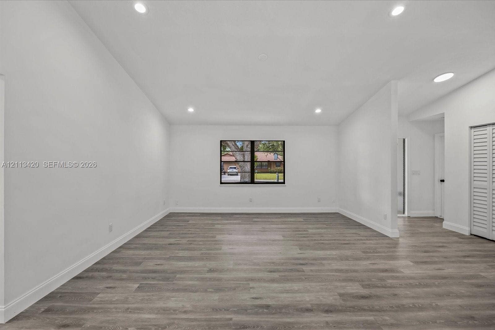 Neutral interior space featuring wood-finish flooring, recessed lighting, vaulted ceilings, and louvered closet doors