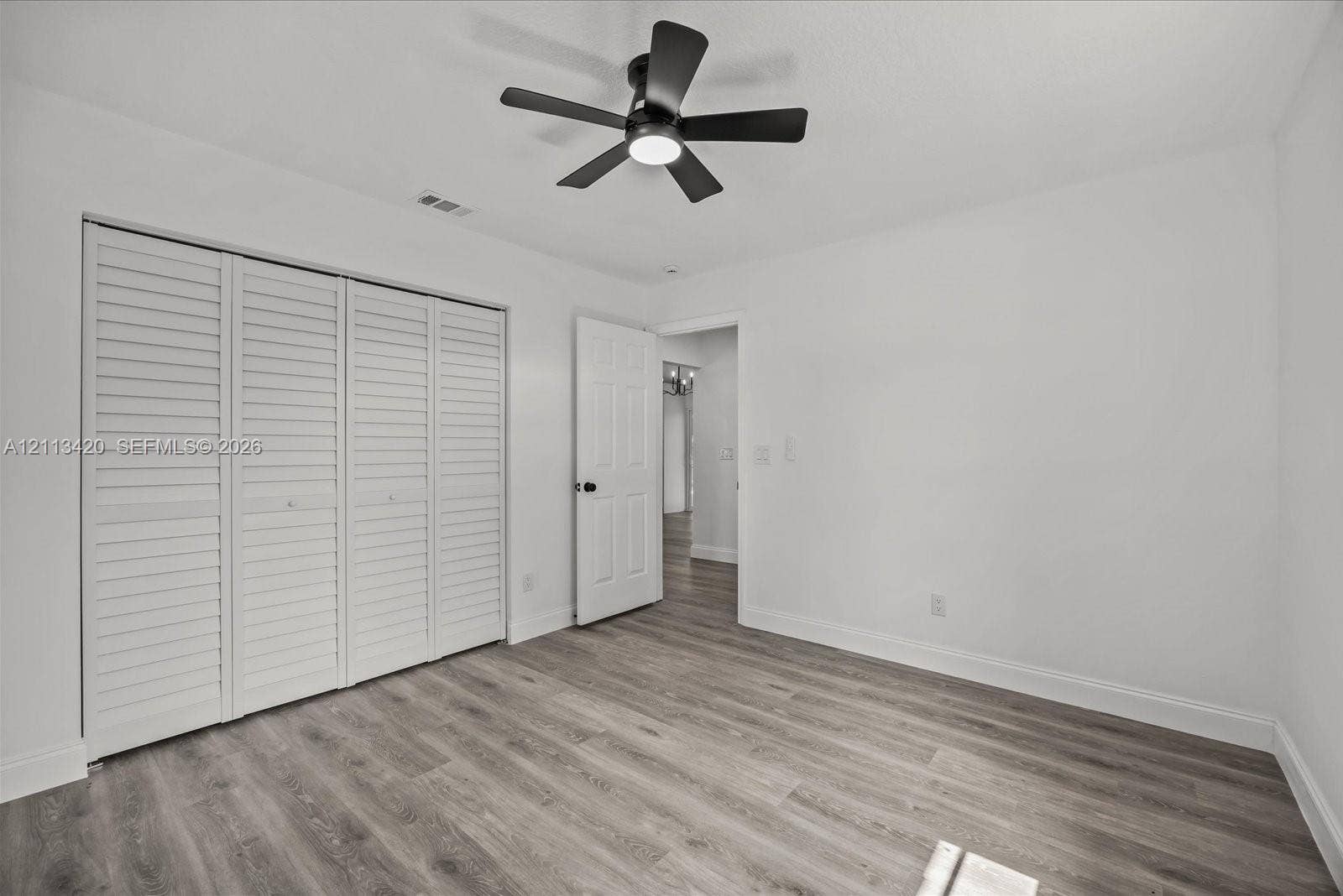 Room featuring wood-finish flooring, a multi-panel louvered closet door, a six-panel interior door, and a matte black ceiling fan with an integrated light fixture