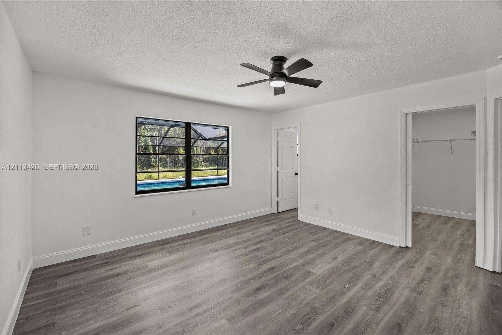 Neutral-toned room featuring wood-finish flooring, a matte black ceiling fan with integrated lighting, and a window with black trim