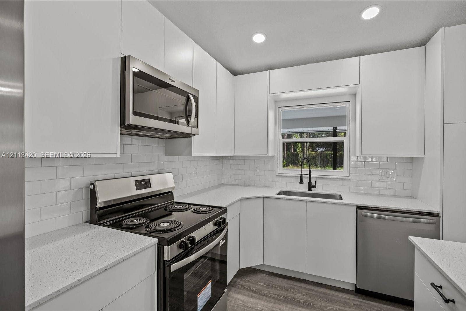 Kitchen featuring white cabinetry, subway tile backsplash, stainless steel appliances, light-toned countertops, and wood-finish flooring