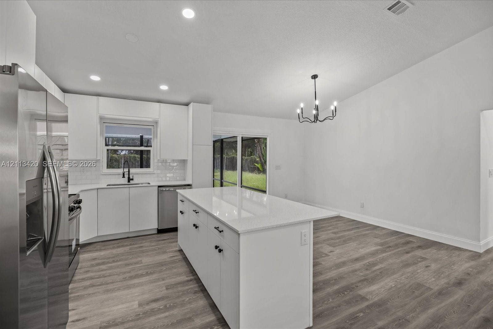 Kitchen featuring a central island with a solid surface countertop, white shaker-style cabinetry, stainless steel appliances, a modern chandelier, and wood-finish flooring