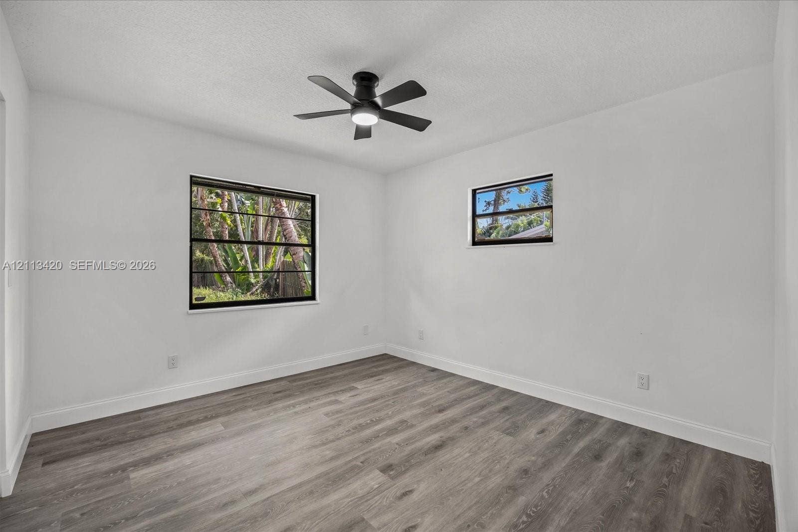 Room featuring wood-finish flooring, white walls, and a ceiling-mounted fan with integrated lighting