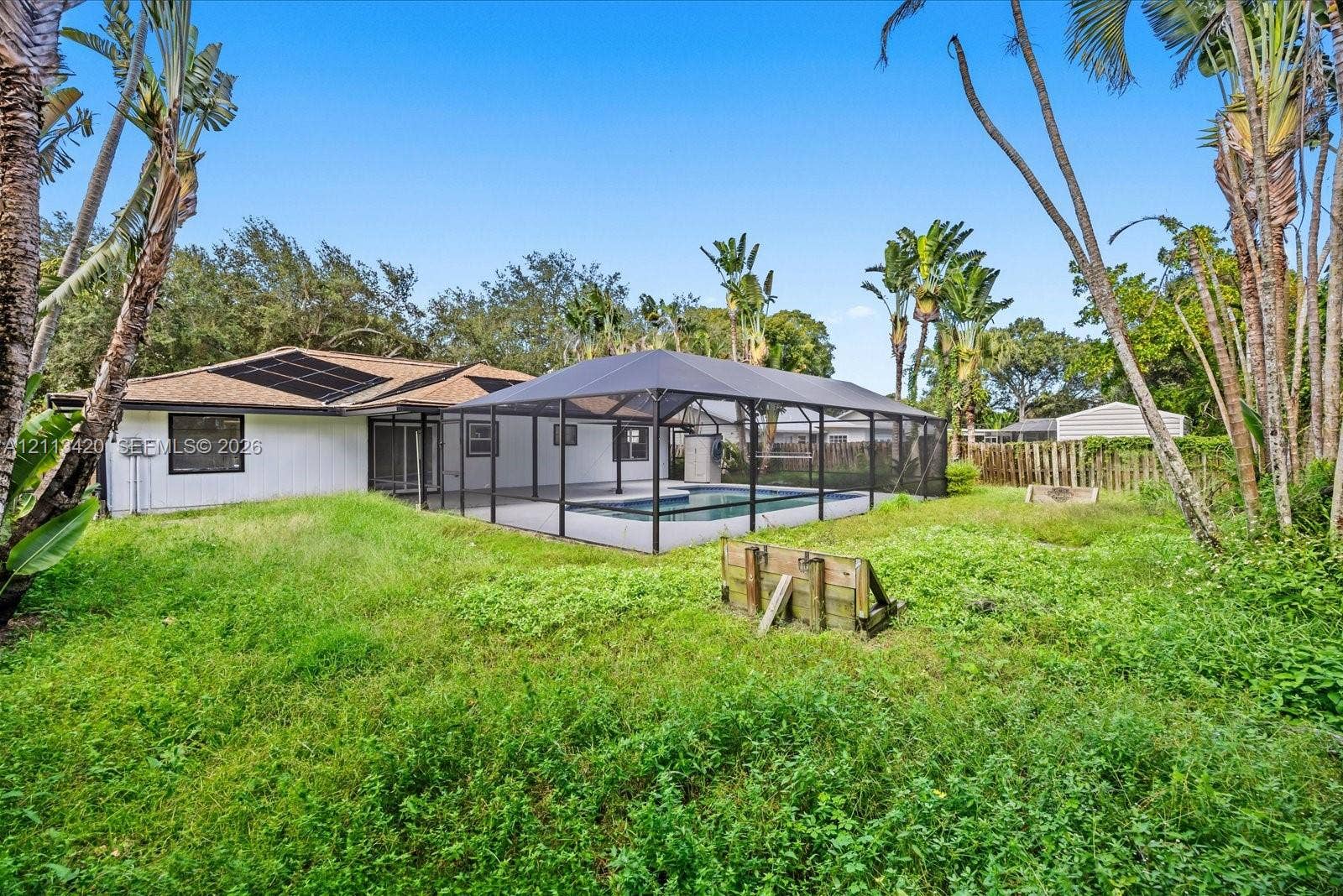 Rear exterior featuring a screen-enclosed pool, solar roof panels, and mature palm trees