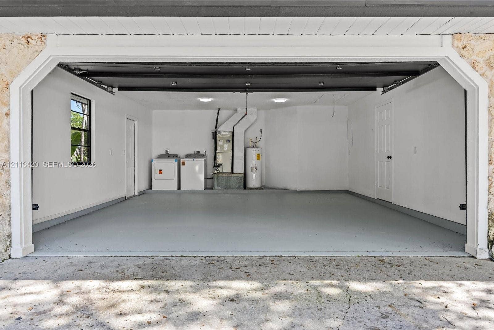 Two-car garage featuring a smooth-finish floor, white walls, dual flush-mount ceiling lights, and integrated laundry hookups