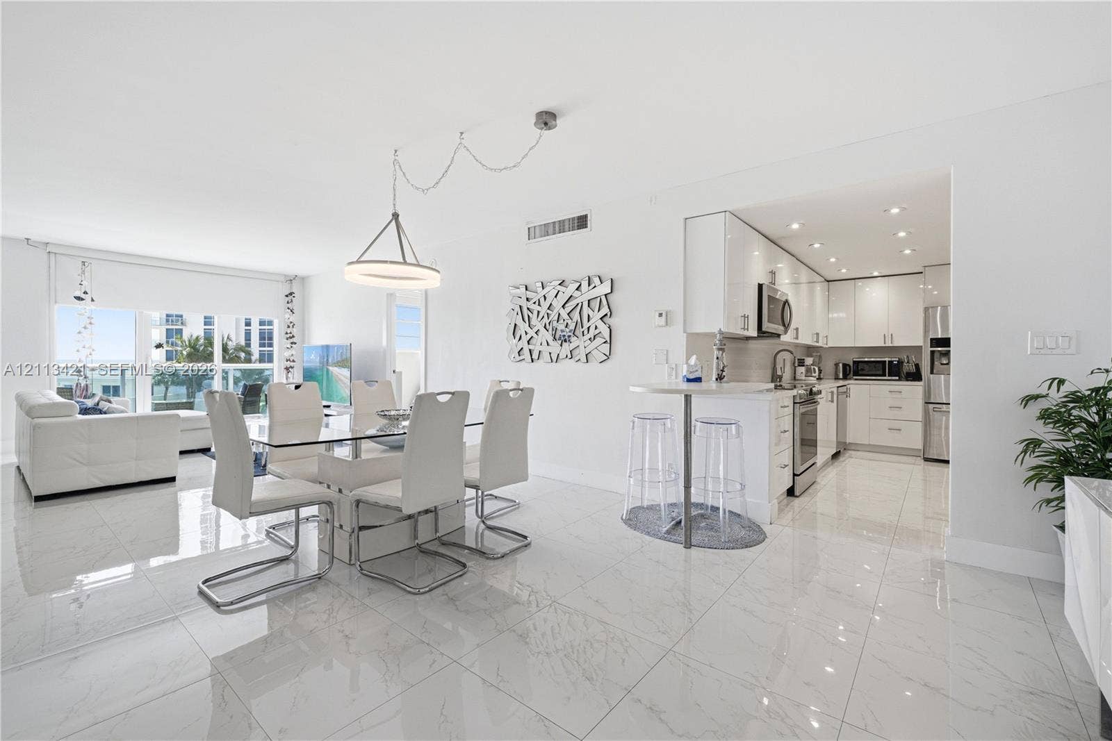3901 S Ocean Drive, #5L, Hollywood, FL 33019 Open-concept area featuring white high-gloss cabinetry, stainless steel appliances, polished stone-finish floor tiling, a peninsula with a breakfast bar, and a modern circular pendant light fixture