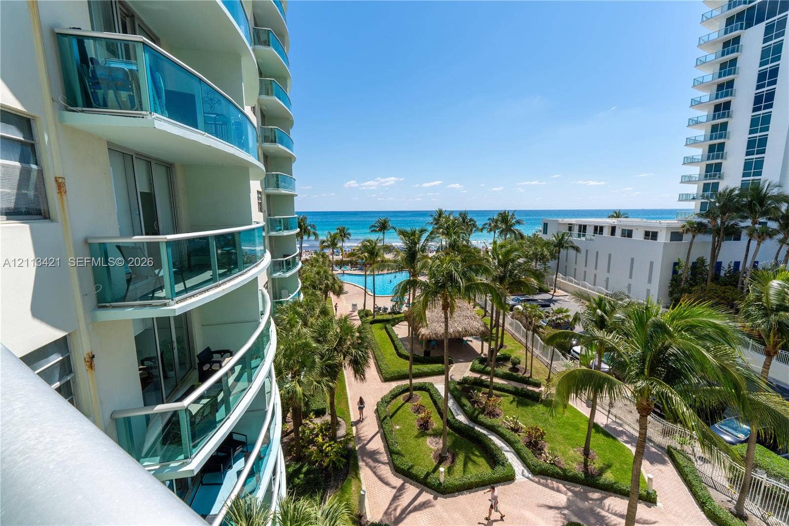 3901 S Ocean Drive, #5L, Hollywood, FL 33019 High-rise building with glass-paneled curved balconies, landscaped courtyards with paved pathways, an outdoor swimming pool, and ocean scenery
