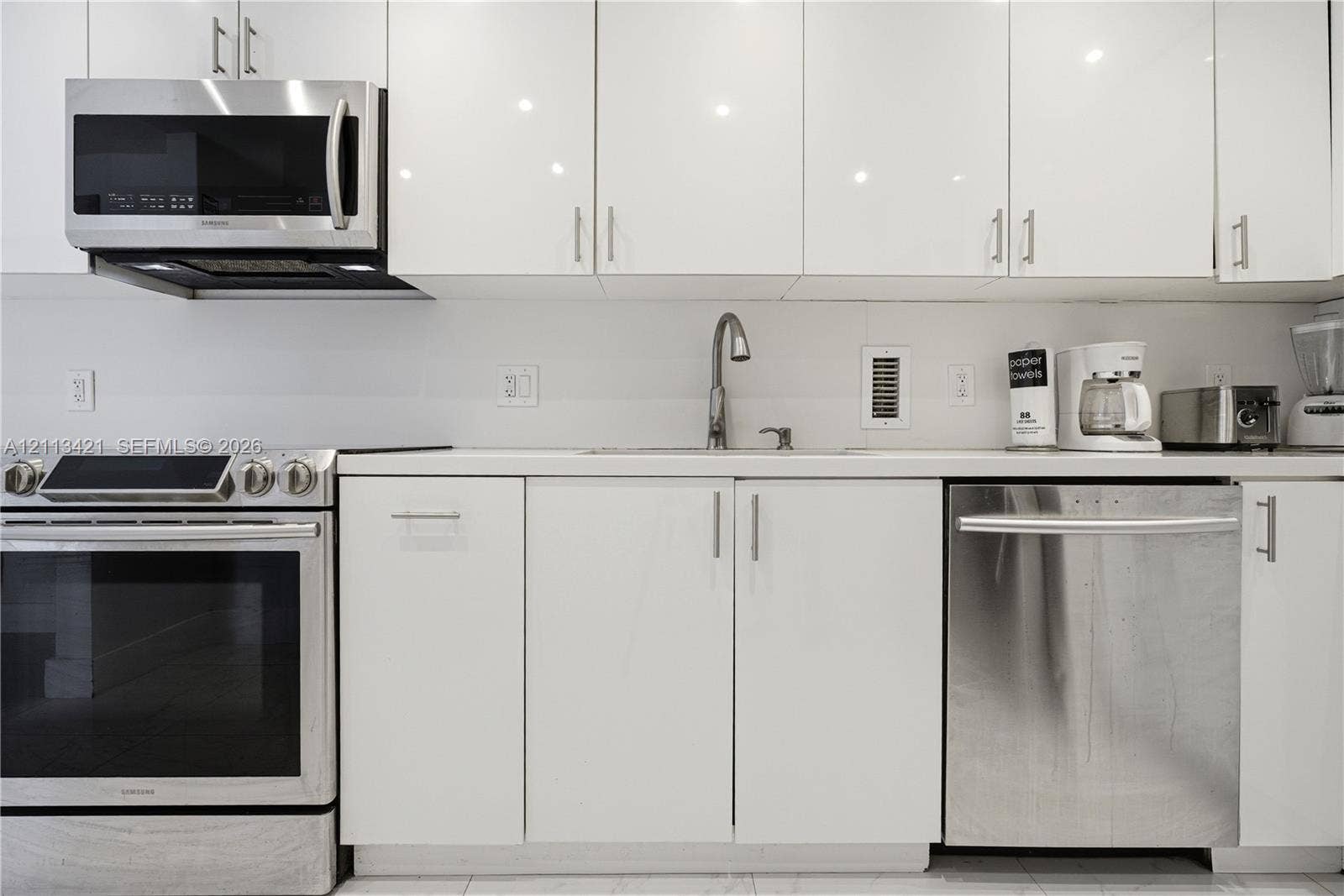 3901 S Ocean Drive, #5L, Hollywood, FL 33019 High-gloss white cabinetry, stainless steel appliances, solid surface countertops, and an undermount sink with a gooseneck faucet