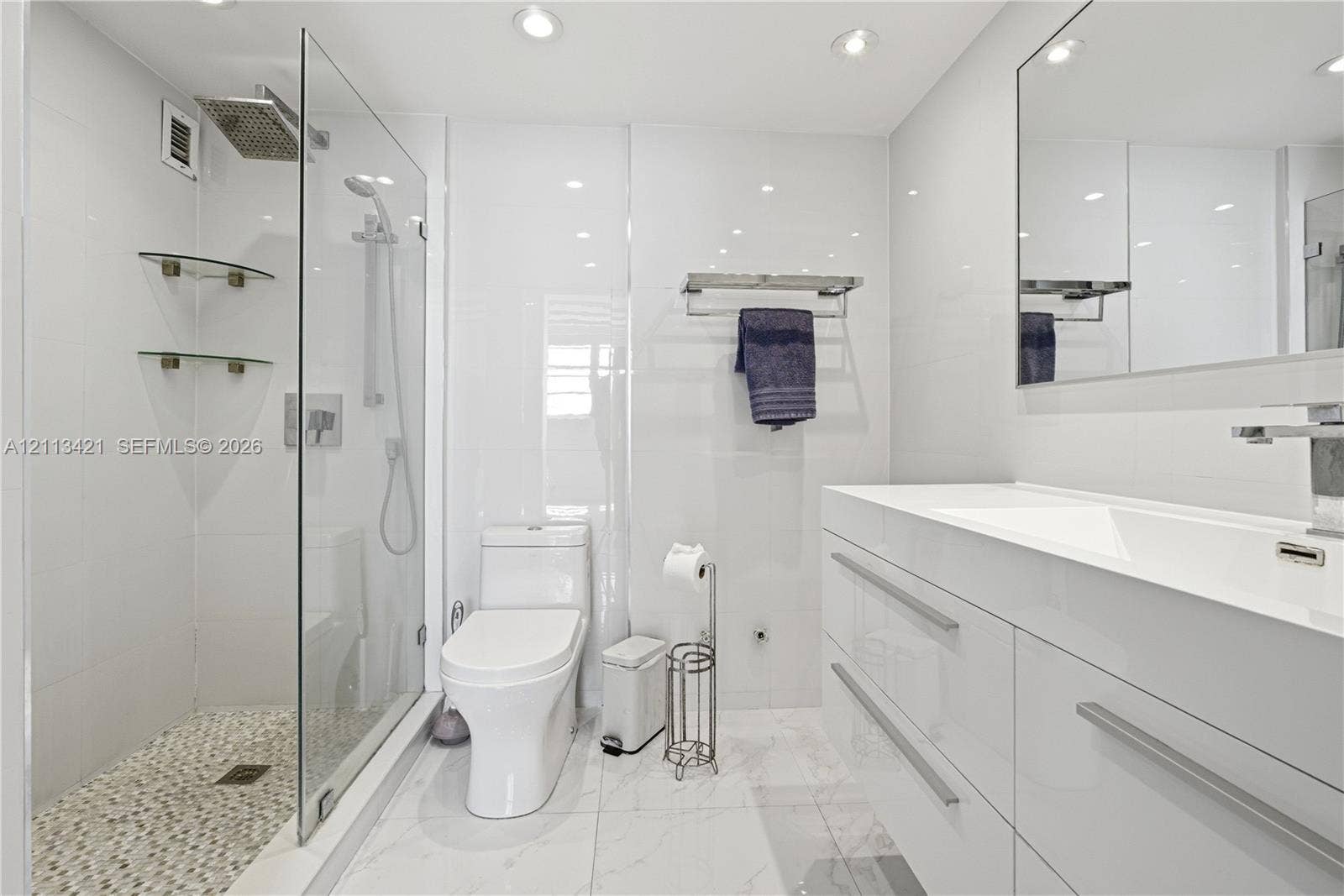 3901 S Ocean Drive, #5L, Hollywood, FL 33019 Modern bathroom featuring a glass-enclosed walk-in shower with rainfall showerhead, pebble-tiled shower floor, gloss-finish floating vanity with integrated sink, and recessed lighting