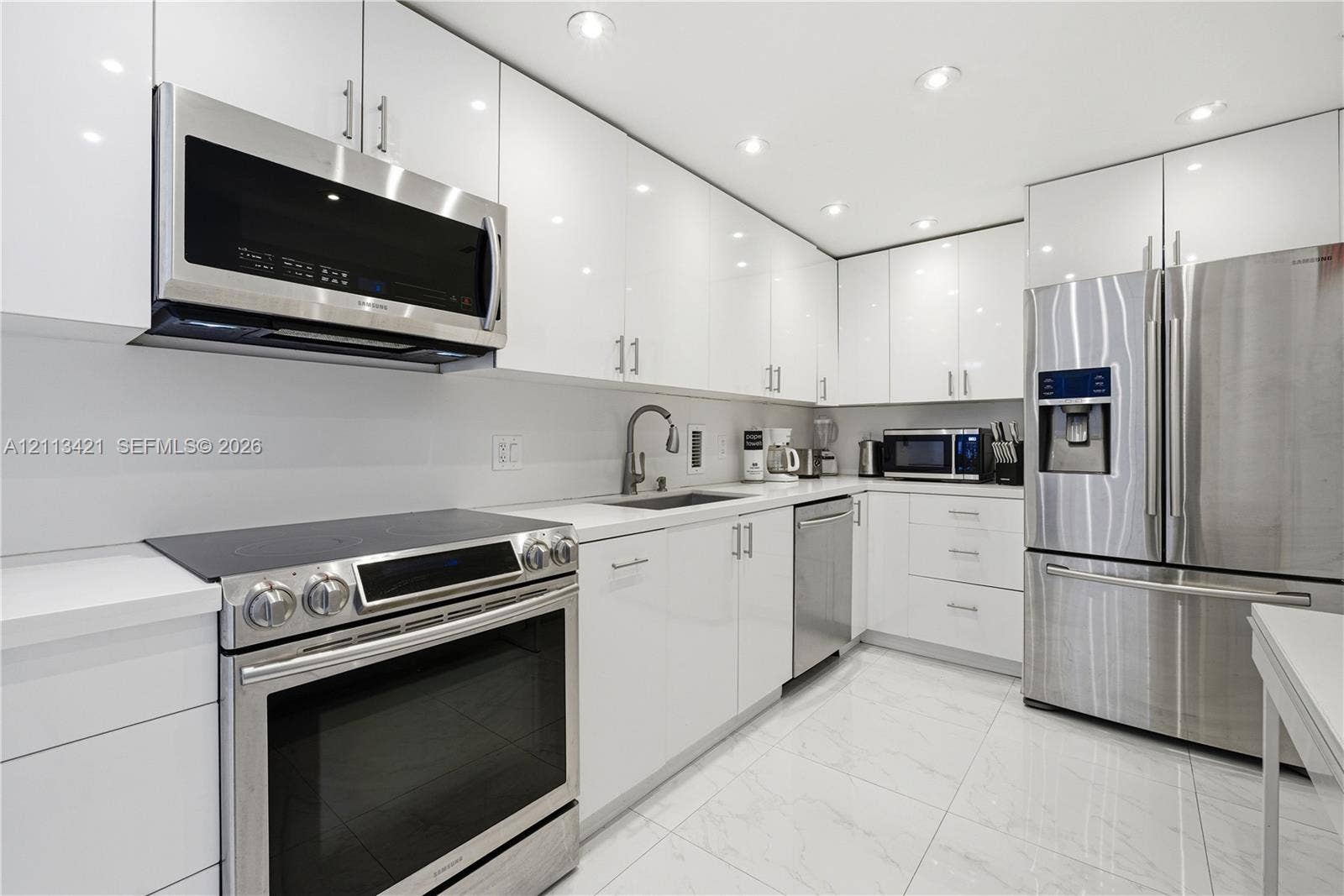 3901 S Ocean Drive, #5L, Hollywood, FL 33019 Modern kitchen featuring high-gloss white cabinetry, quartz countertops, stainless steel appliances, and large-format tile flooring