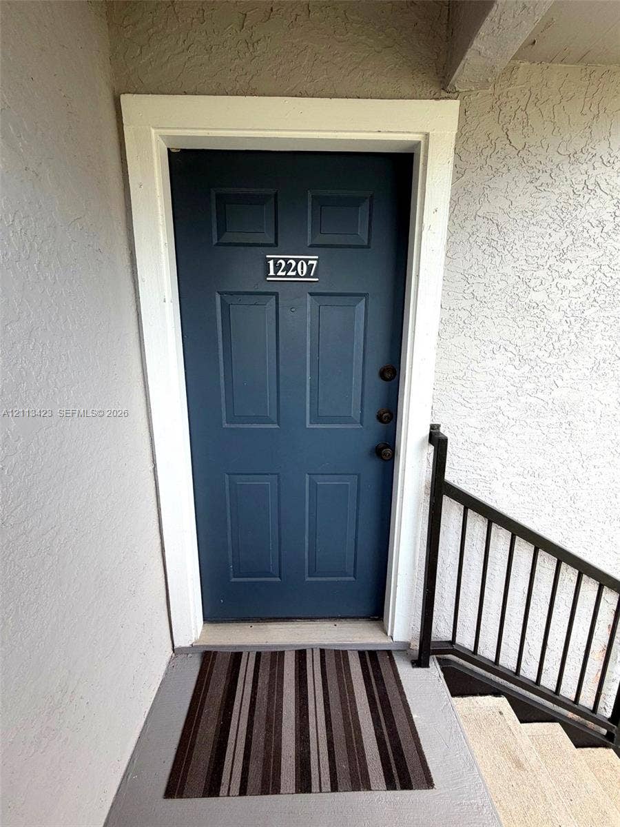 10360 SW 150th Court, #12207, Miami, Miami, FL 33196 Exterior entryway featuring a solid blue door with six panels, white door casing, and a black metal handrail