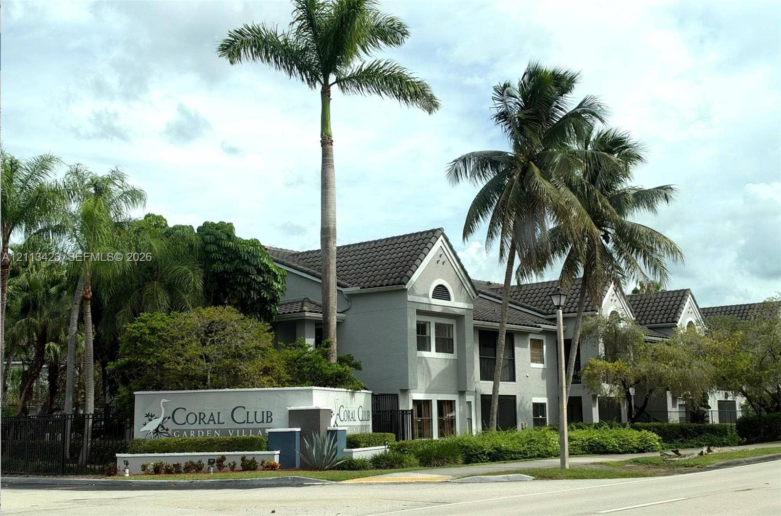 10360 SW 150th Court, #12207, Miami, Miami, FL 33196 Multi-unit stucco building featuring a tile roof, screened-in balconies, mature palm trees, and professionally manicured landscaping