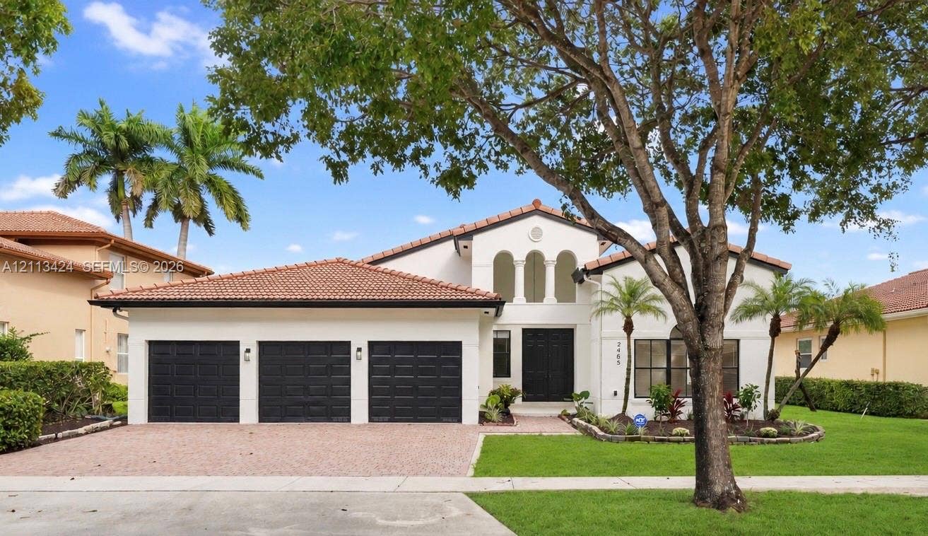 2465 SW 132nd Terrace, Miramar, FL 33027 Stucco exterior featuring a clay tile roof, three-car garage, arched architectural detailing, and landscaped grounds