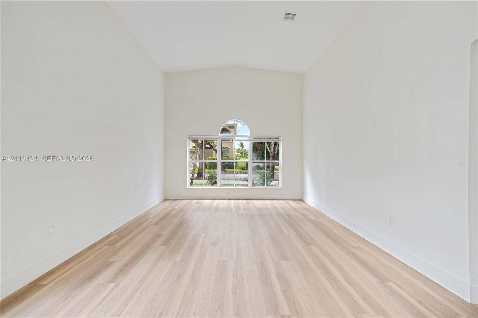 2465 SW 132nd Terrace, Miramar, FL 33027 Vaulted ceiling featuring a multi-paned window with an arched transom, complemented by light-toned wood-finish flooring