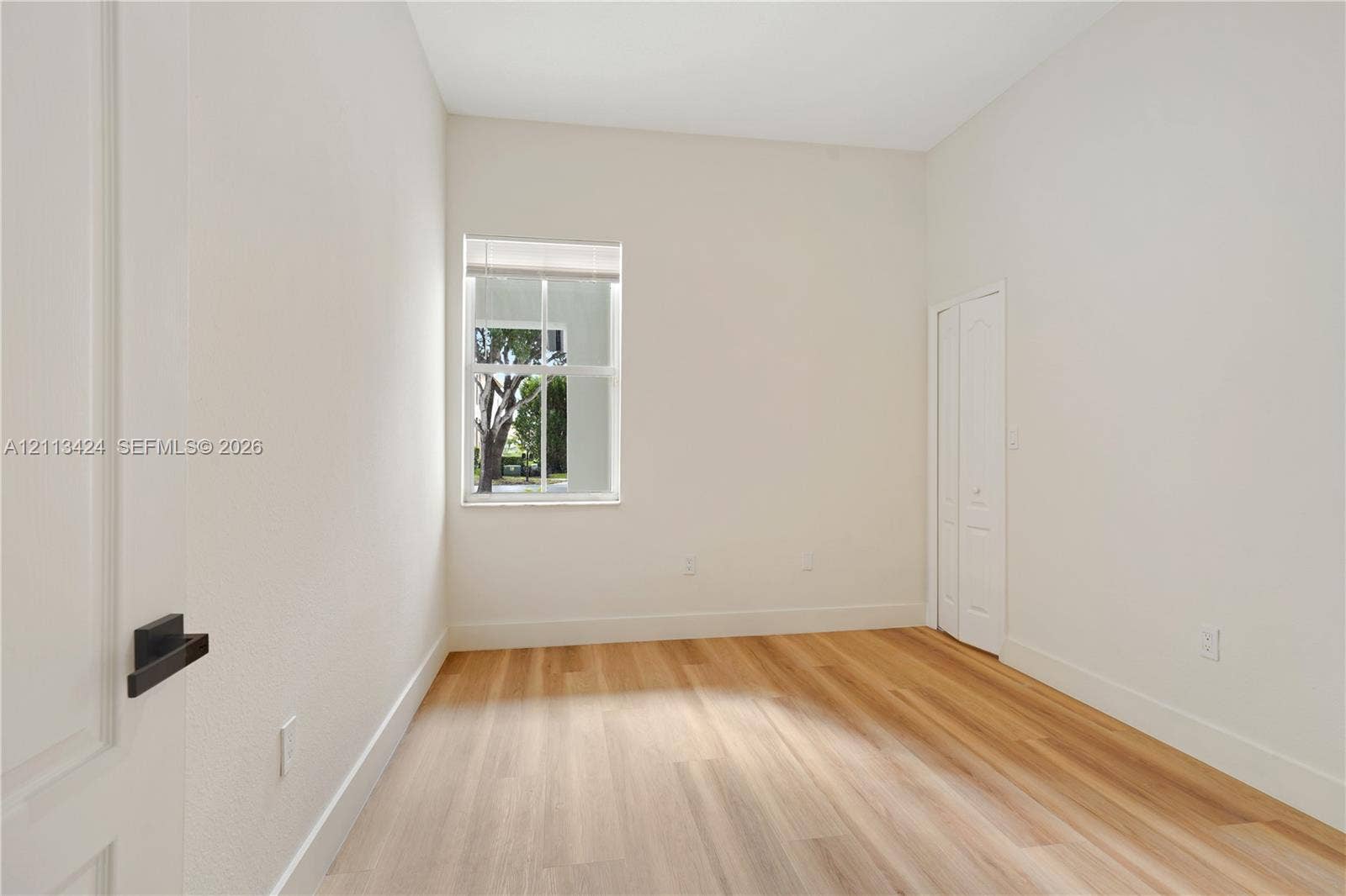 2465 SW 132nd Terrace, Miramar, FL 33027 Interior space featuring wood-finish flooring, crisp white walls, a single-pane window with interior muntins, and dual-panel closet doors with matte black hardware