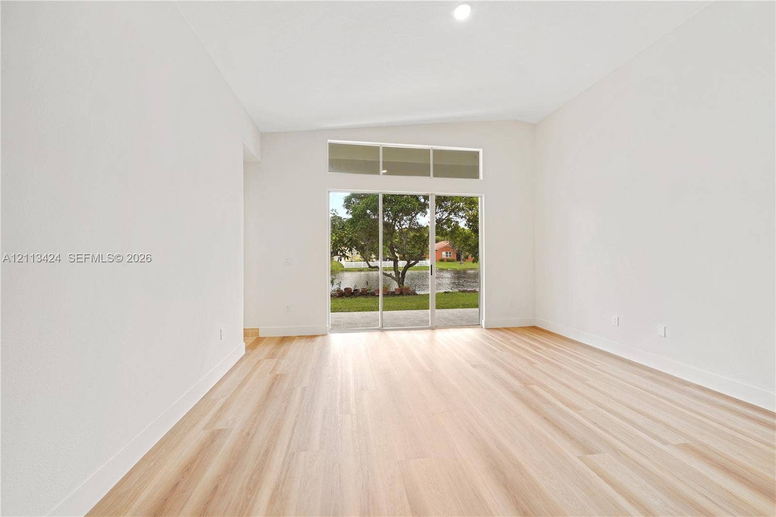 2465 SW 132nd Terrace, Miramar, FL 33027 Interior space featuring vaulted ceilings, light-toned wood-finish flooring, and expansive sliding glass doors topped with rectangular transom windows