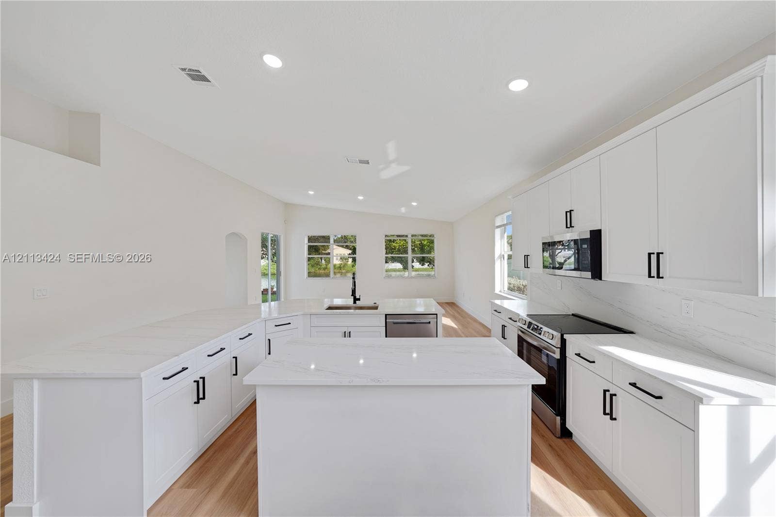 2465 SW 132nd Terrace, Miramar, FL 33027 Kitchen featuring white shaker-style cabinetry, quartz countertops with a waterfall-edge center island, integrated stainless steel appliances, and wood-finish flooring