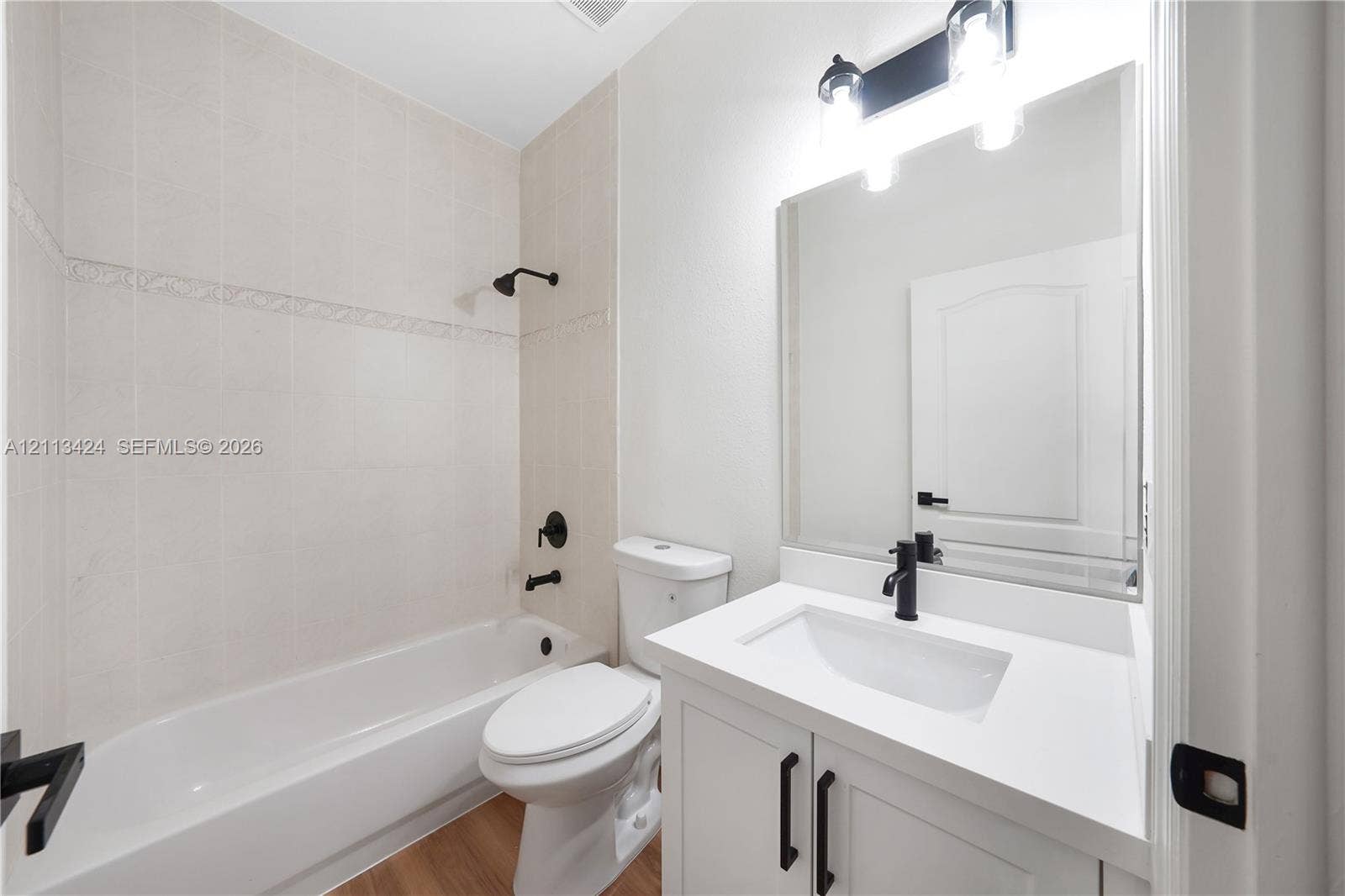 2465 SW 132nd Terrace, Miramar, FL 33027 Bathroom featuring a white vanity with a rectangular basin, matte black faucet, full-width vanity mirror, wood-finish flooring, and a tub-shower combination with light-toned tile surround