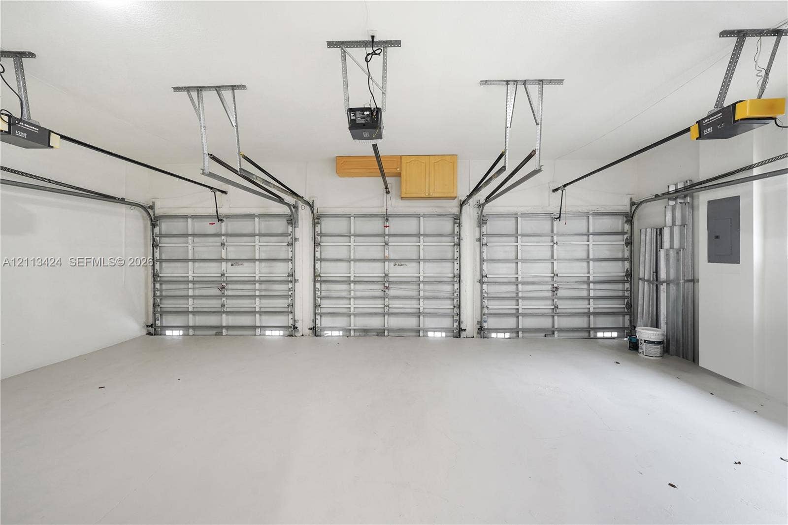 2465 SW 132nd Terrace, Miramar, FL 33027 Three-car garage featuring finished concrete flooring, three overhead door tracks, ceiling-mounted automatic door openers, and wall-mounted cabinetry