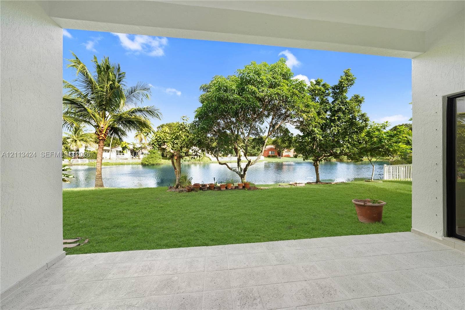 2465 SW 132nd Terrace, Miramar, FL 33027 Covered patio with tile flooring featuring expansive water frontage, a manicured lawn, and mature trees