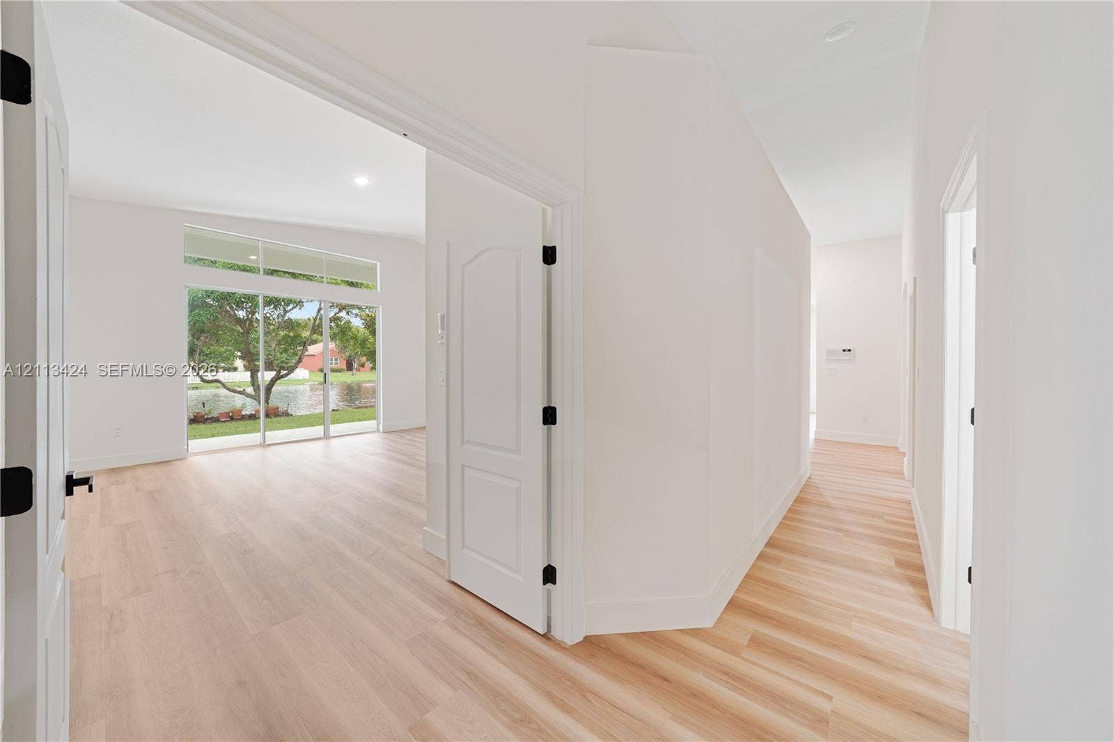 2465 SW 132nd Terrace, Miramar, FL 33027 Interior featuring light-toned wood-finish flooring, high ceilings, arched-top interior doors with matte black hardware, and floor-to-ceiling glass sliding doors