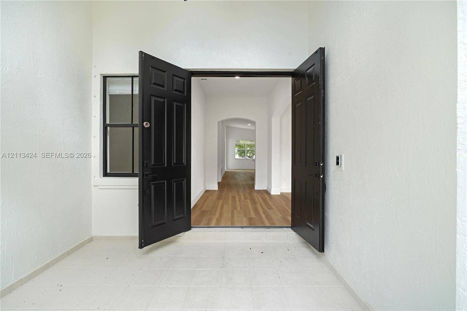 2465 SW 132nd Terrace, Miramar, FL 33027 Double front entry doors with black finish, white textured wall exterior, single-pane side window, and interior wood-finish flooring