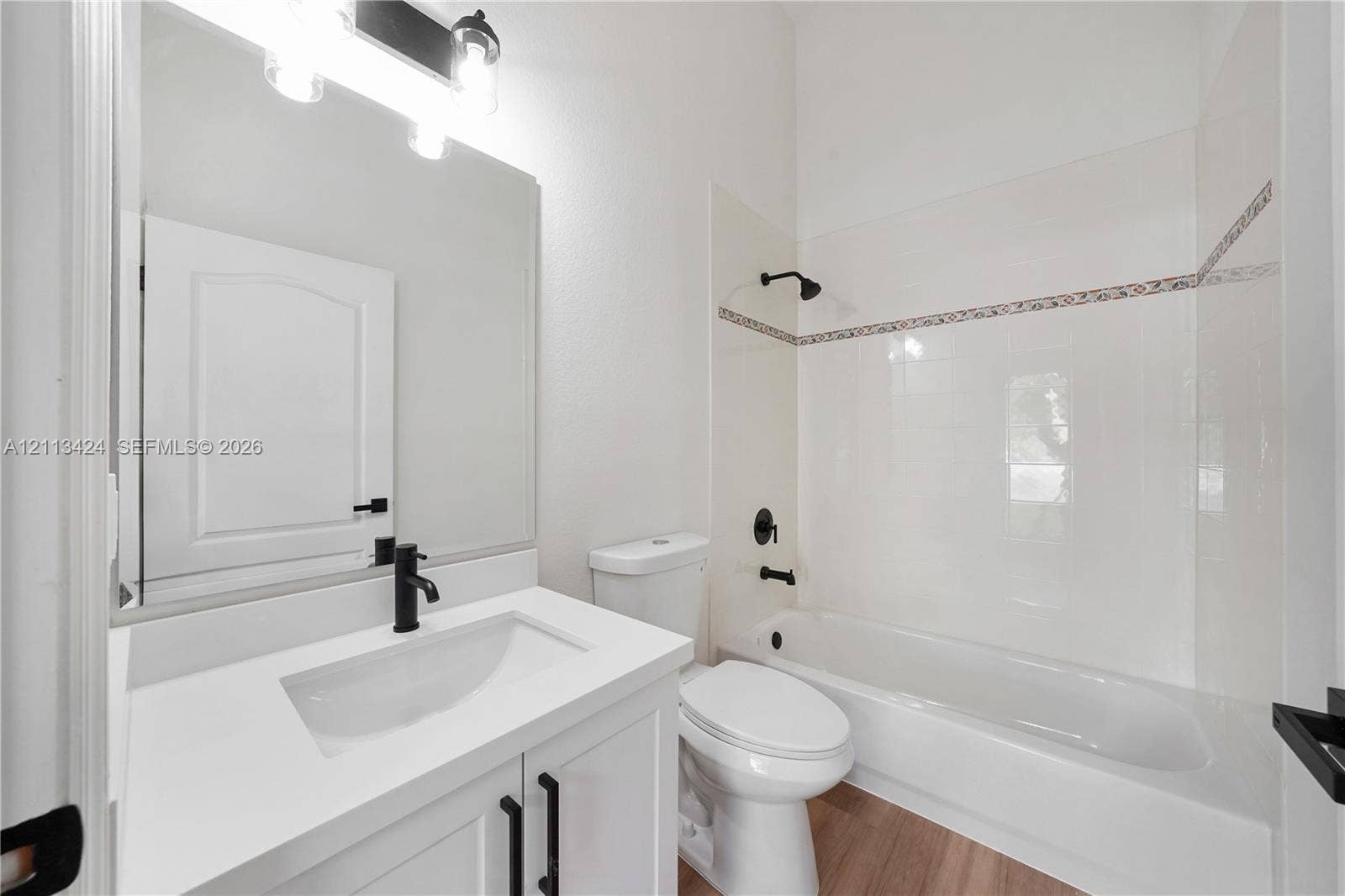 2465 SW 132nd Terrace, Miramar, FL 33027 Bathroom featuring a white vanity with a composite countertop, matte black fixtures, a wall-mounted light fixture, and a tub-shower combination with decorative tile inlay