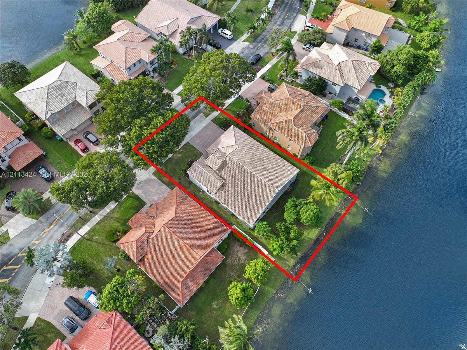 2465 SW 132nd Terrace, Miramar, FL 33027 Aerial perspective featuring a waterfront lot, multi-hipped tile roof, paved driveway, and mature landscaping
