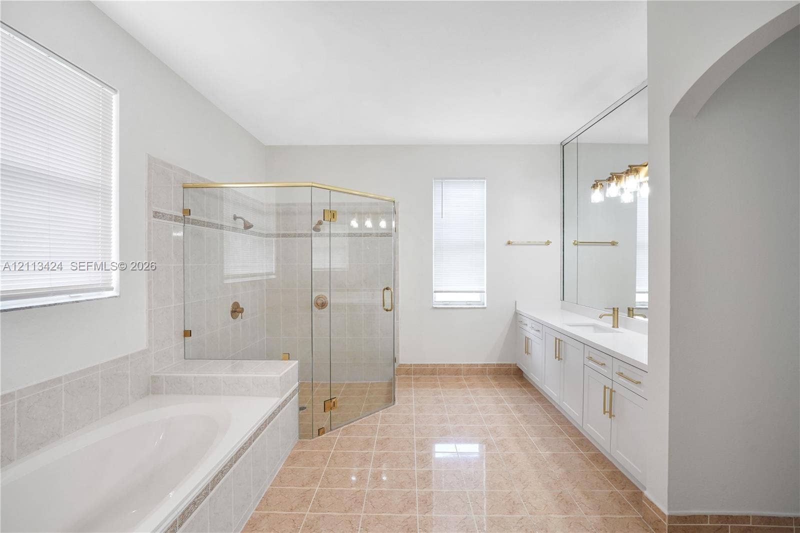 2465 SW 132nd Terrace, Miramar, FL 33027 Bathroom featuring a glass-enclosed shower, soaking tub with tile surround, dual-sink vanity with white cabinetry, and large-format wall mirror