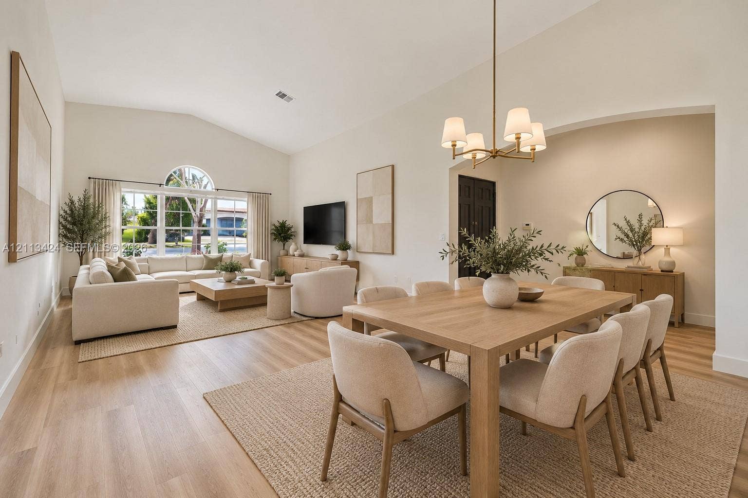 2465 SW 132nd Terrace, Miramar, FL 33027 virtually staged Open-concept living space featuring vaulted ceilings, wood-finish flooring, a multi-pane window with an arched transom, and an overhead multi-arm chandelier