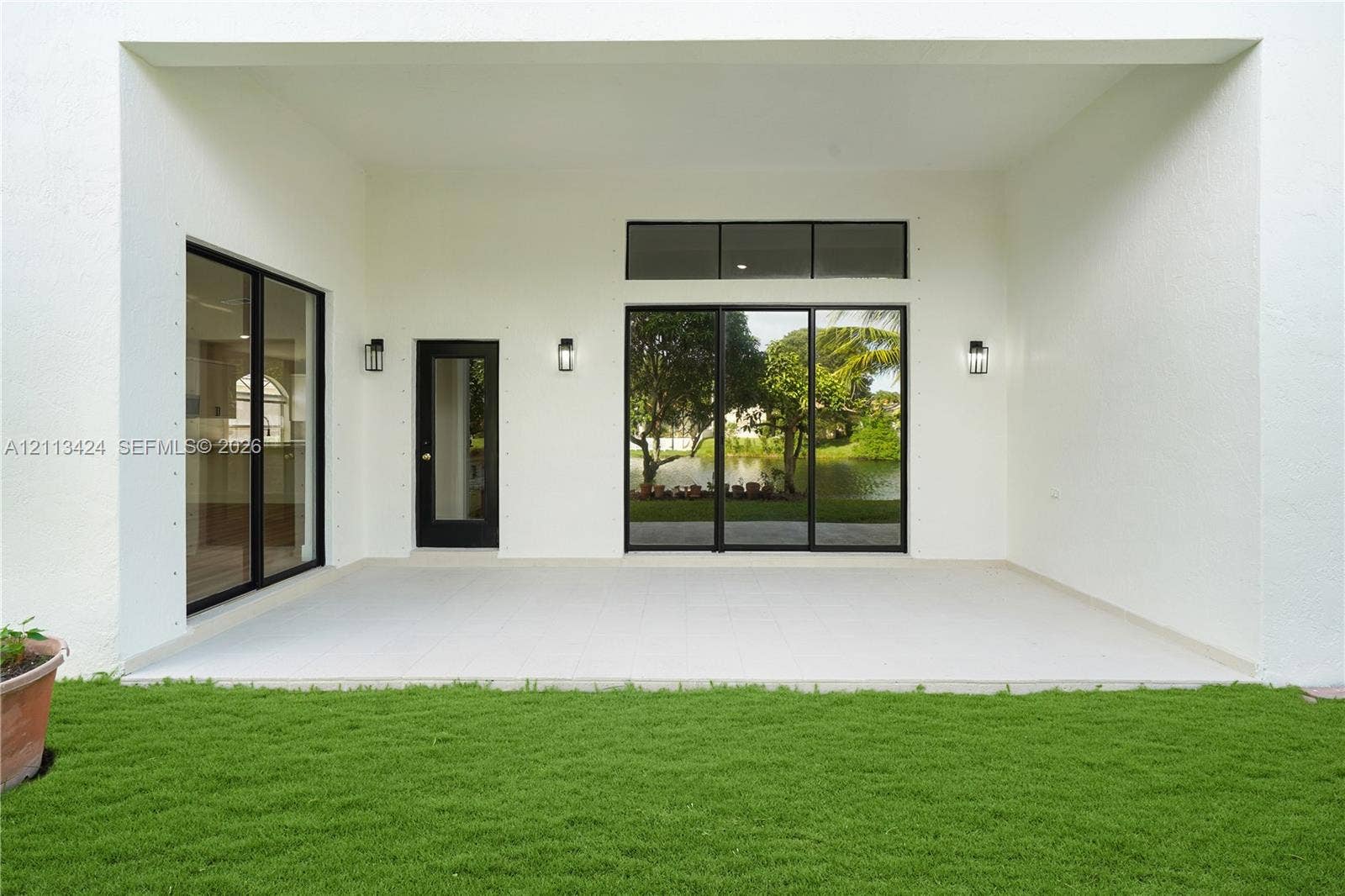 2465 SW 132nd Terrace, Miramar, FL 33027 Covered patio featuring large-format tile flooring, multi-panel sliding glass doors, a transom window, and wall-mounted exterior lighting