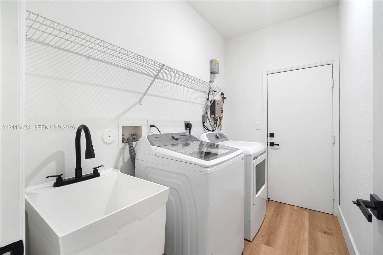 2465 SW 132nd Terrace, Miramar, FL 33027 Laundry room featuring wood-finish flooring, a utility sink with a matte black faucet, and an integrated wire wall shelf