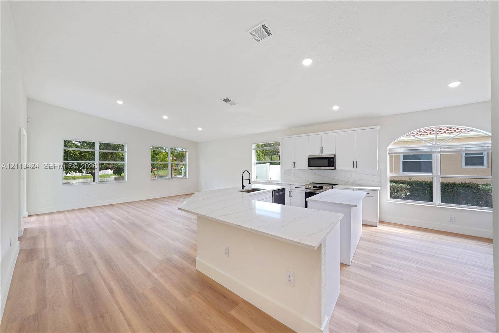 2465 SW 132nd Terrace, Miramar, FL 33027 Open-concept kitchen and living area featuring wood-finish flooring, a quartz-topped peninsula, recessed lighting, white cabinetry, and an arched window