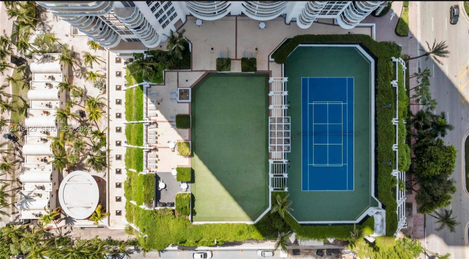 6365 Collins Avenue, #909, Miami Beach, FL 33141 Aerial recreation deck featuring a hard-court tennis surface, synthetic turf lawn, white pergola structure, and landscaped perimeter hedging
